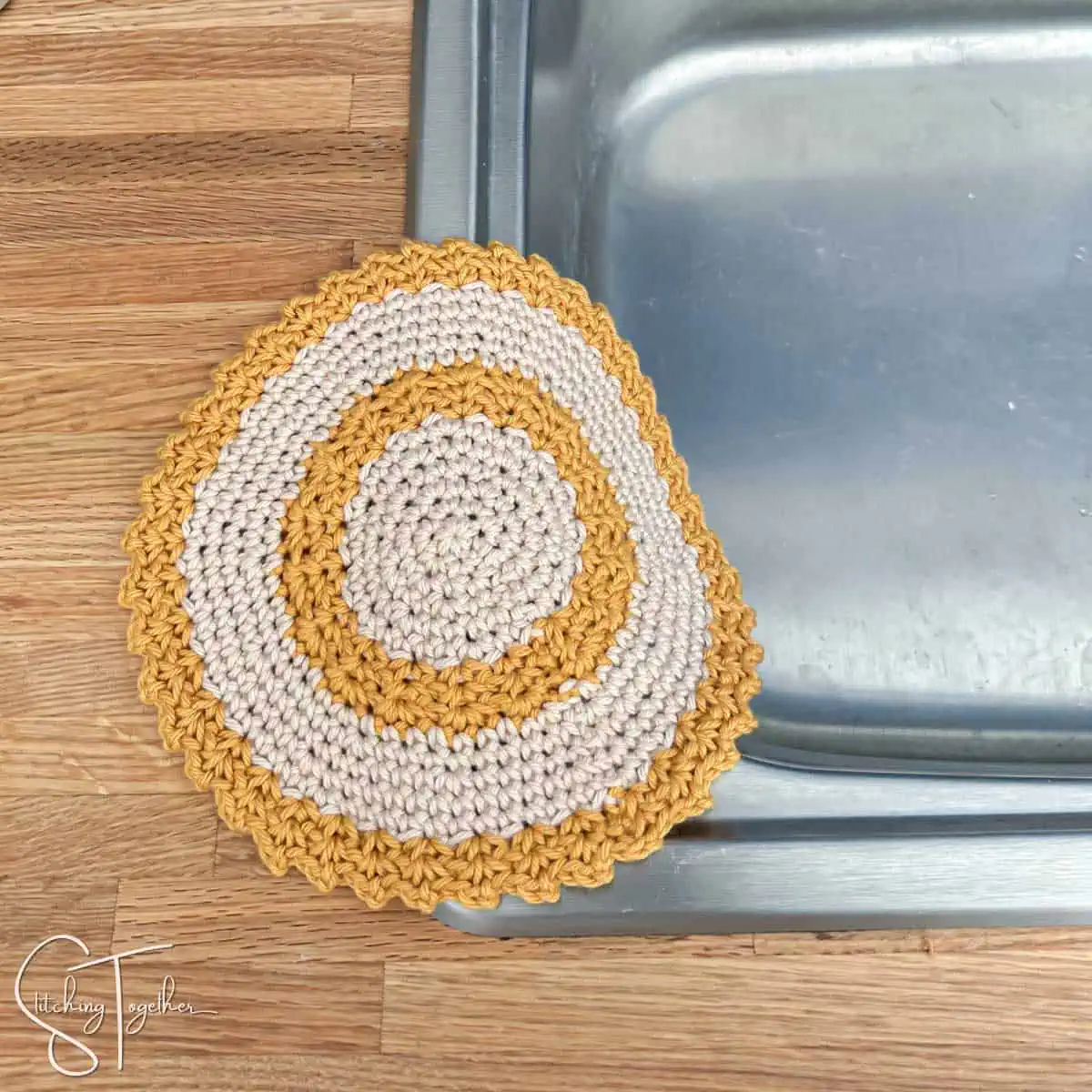 yellow and cream round crochet dishcloth draped on the side of a sink