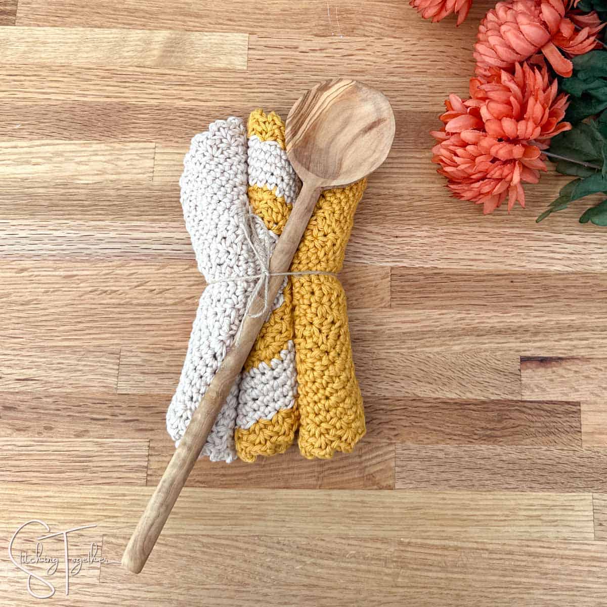 three dishcloths rolled up and tied with jute with a wooden spoon on top