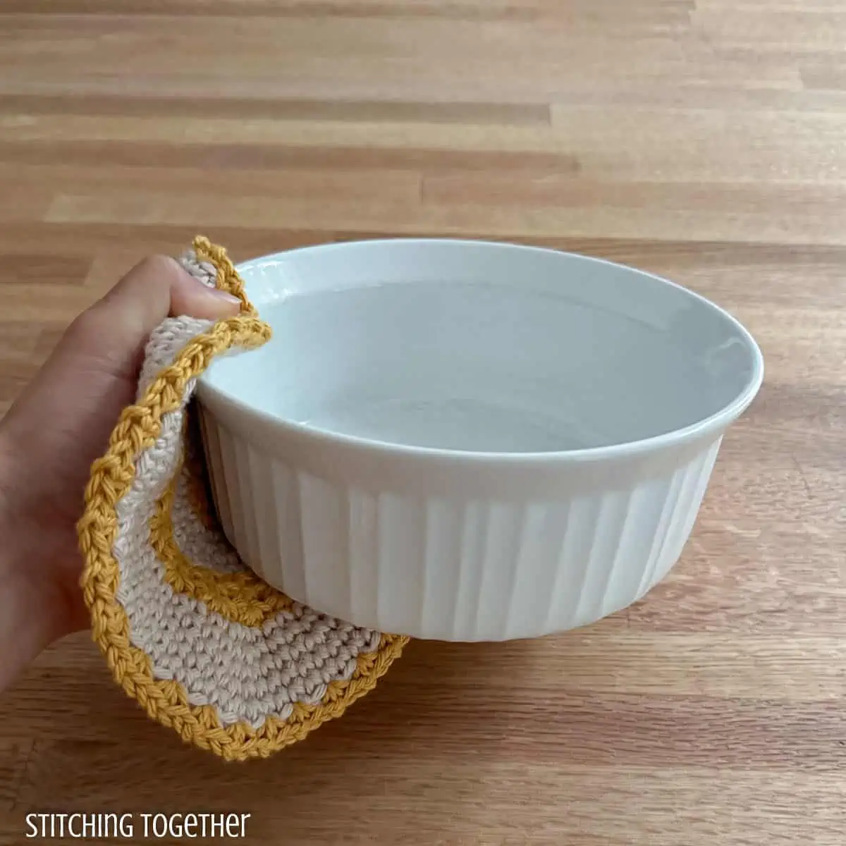 hand holding a white dish with a crochet potholder