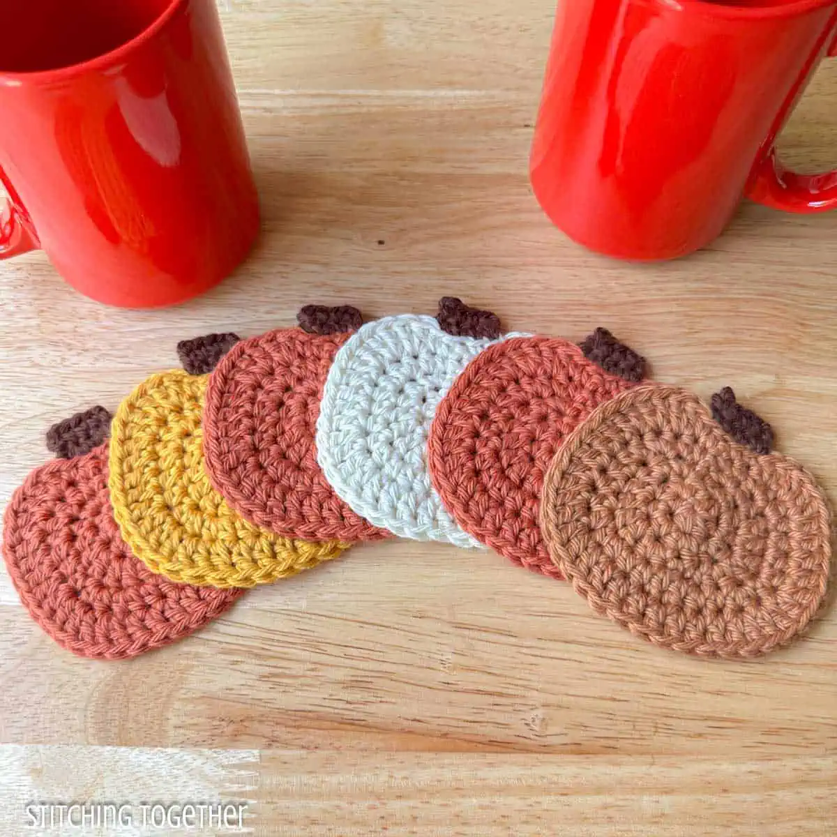 two red mugs with six colorful crochet pumpkins spread in front of them