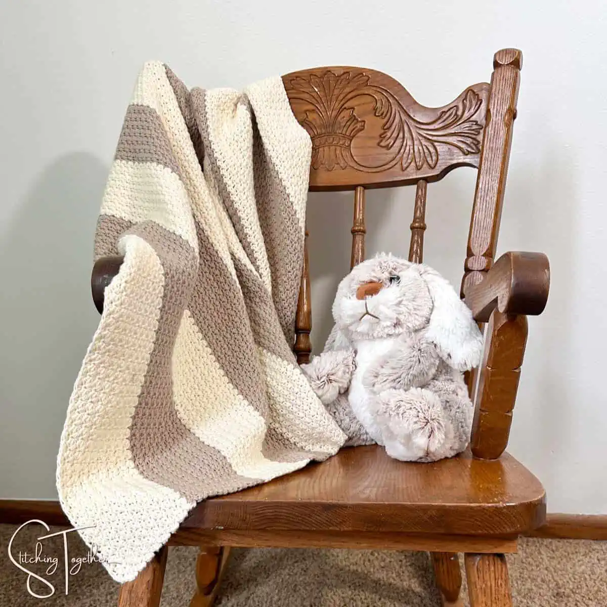 striped crochet baby blanket draped over the arm of a small rocking chair with a stuffed bunny on the seat