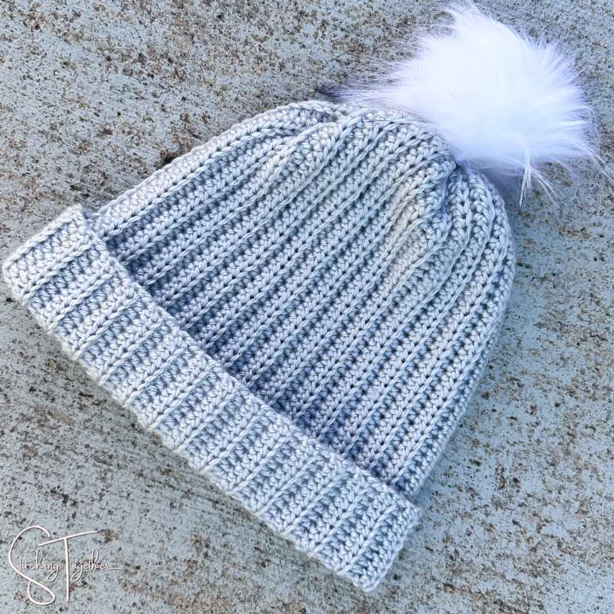 gray crochet ribbed hat with a white pom pom laying on the ground