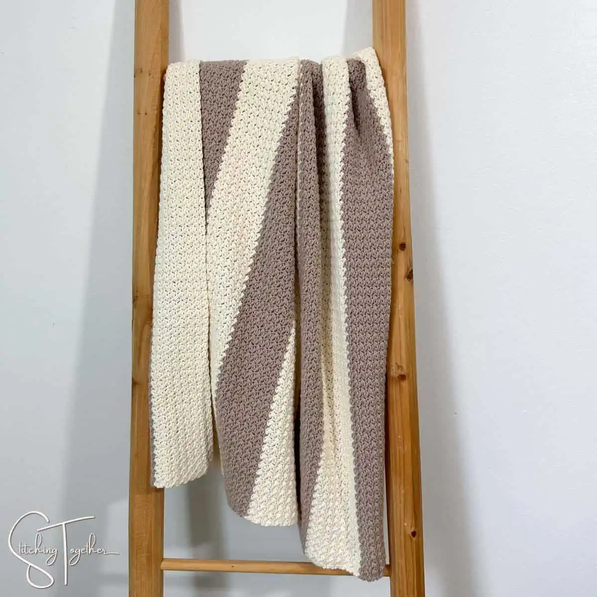 striped crochet suzette stitch baby blanket draped on a blanket ladder