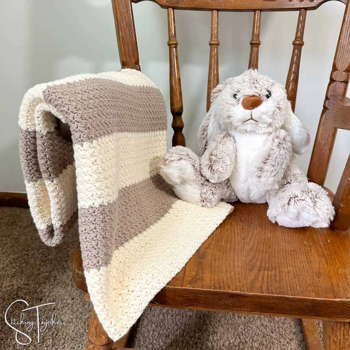 crochet baby blanket folded over the arm of a small rocking chair with a stuffed bunny on the seat