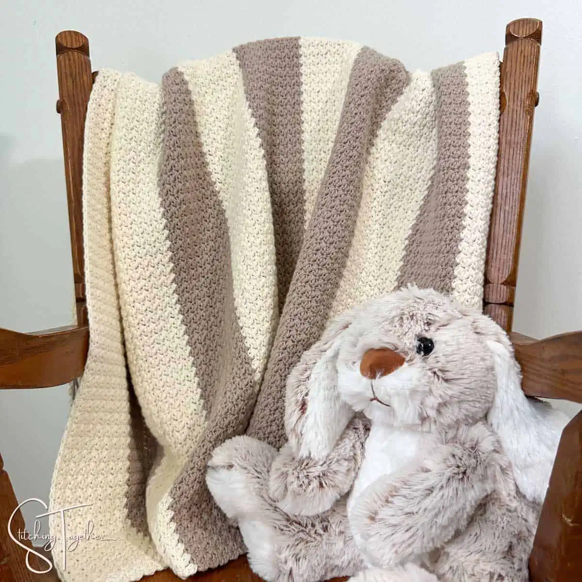 striped crochet blanket draped over the back of a small rocking chair with a stuffed bunny on the seat