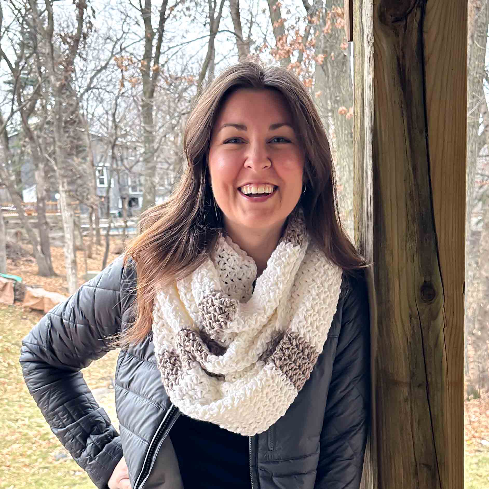 woman wearing a white and tan striped crochet scarf while leaning against beam