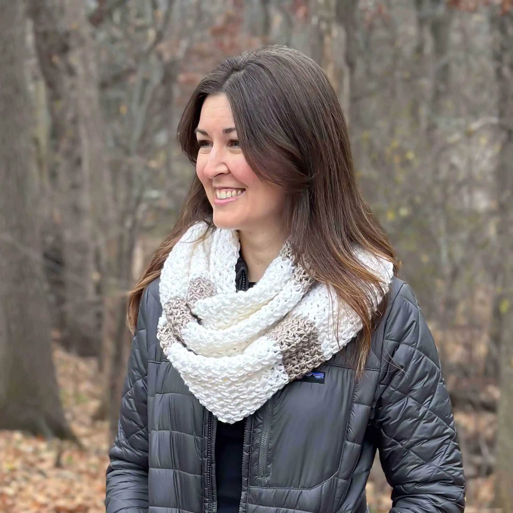 smiling woman outside wearing a white and tan striped and textured crochet infinity scarf