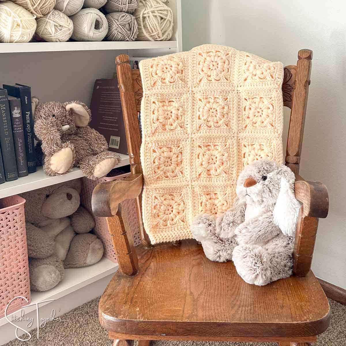 granny square blanket folded on the back of a small rocking chair with a stuffed bunny sitting on the chair