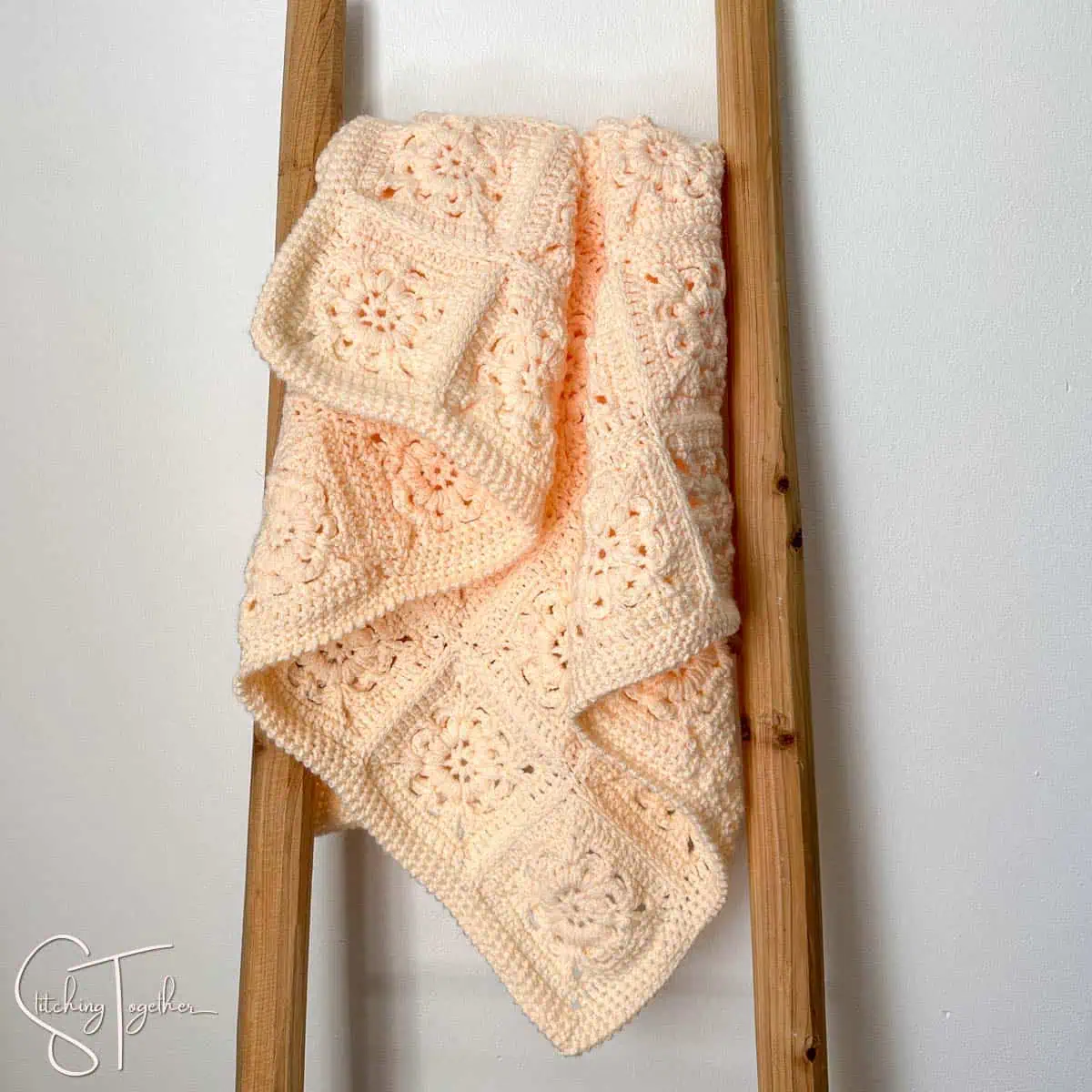 crochet peach colored baby blanket draped on a ladder