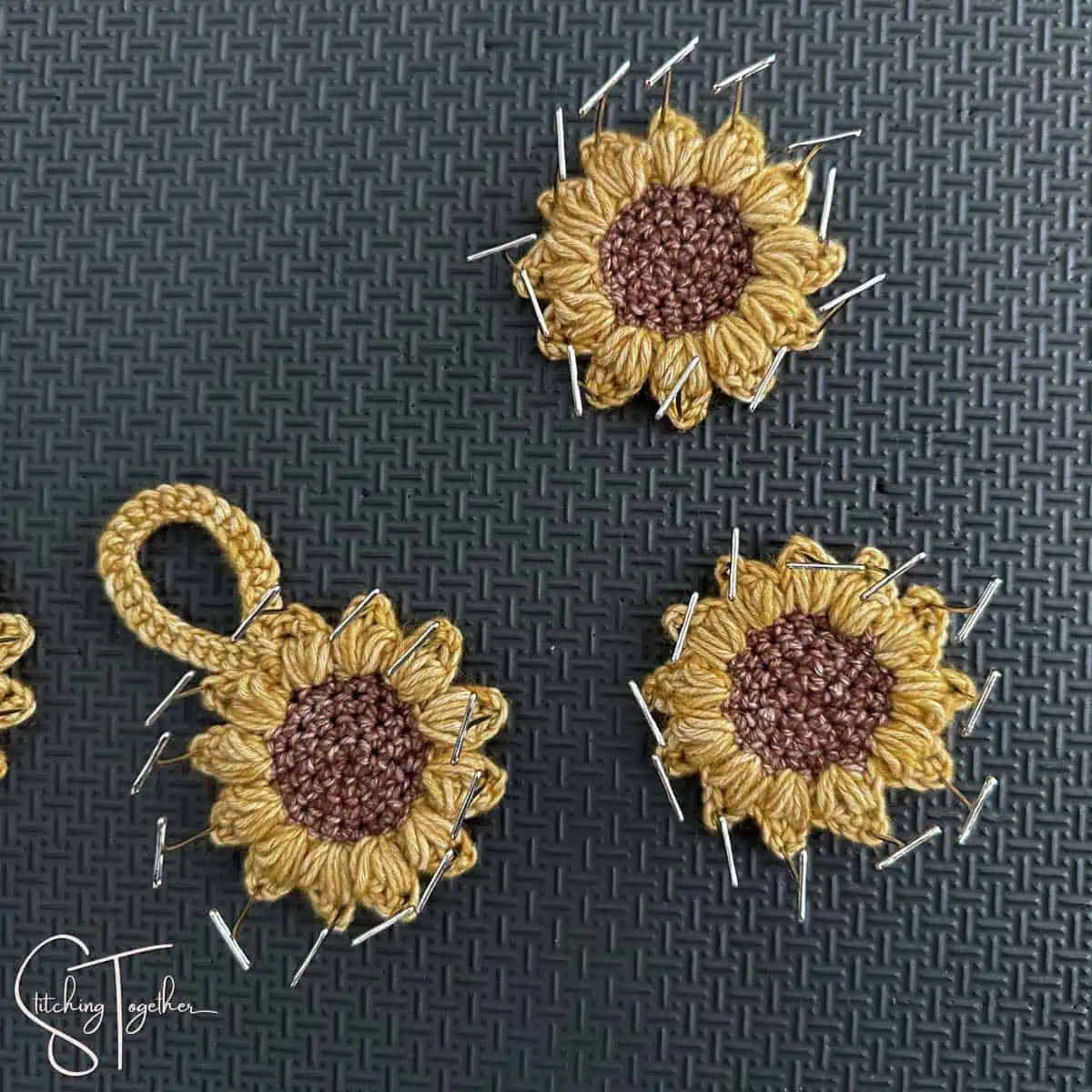 3 crocheted sunflowers pinned on a blocking board