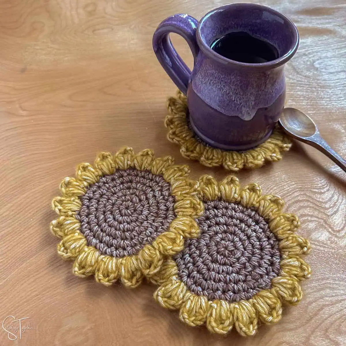 a coffee mug and spoon sitting on a sunflower crochet coaster with other coasters stacked