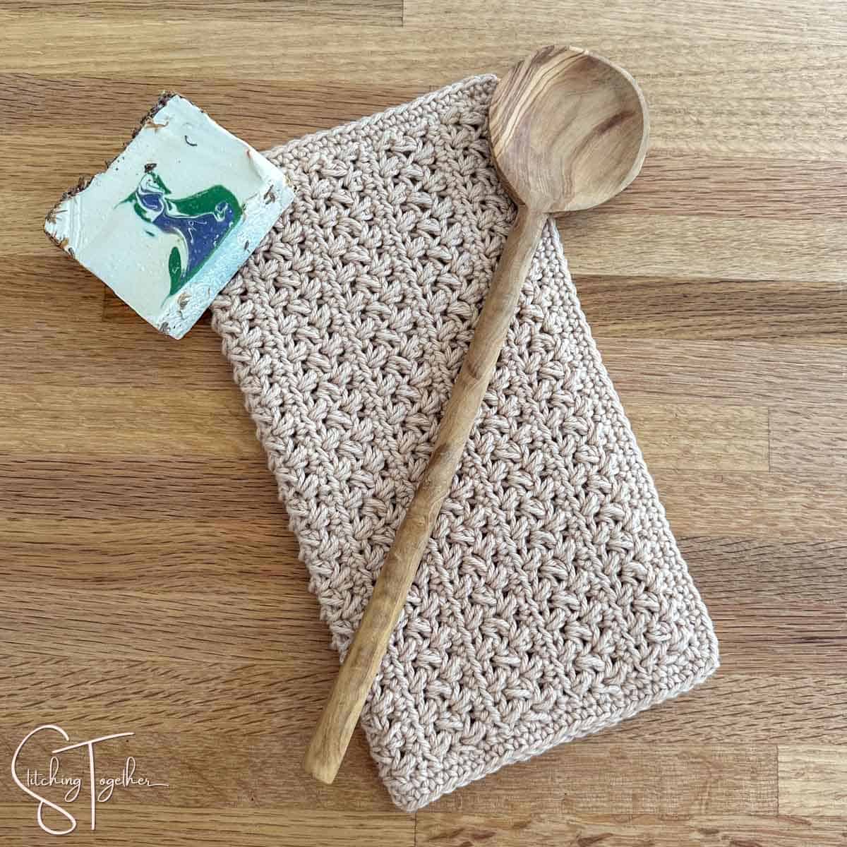 farmhouse dishcloth that's folded in half with a wooden spoon and a bar of soap laying on top