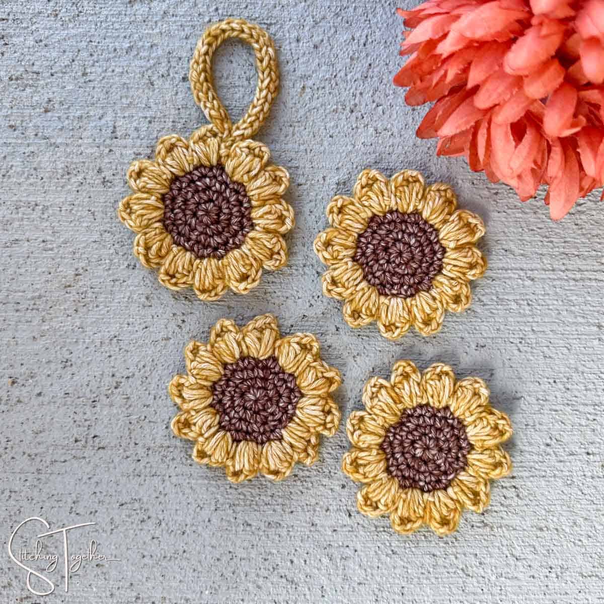 four small crochet sunflowers laying next to an orange flower
