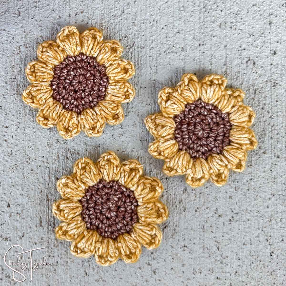 close up of three small crochet sunflowers laying flat