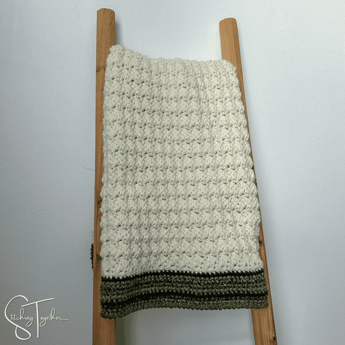 textured crochet baby blanket folded and hanging on a blanket ladder