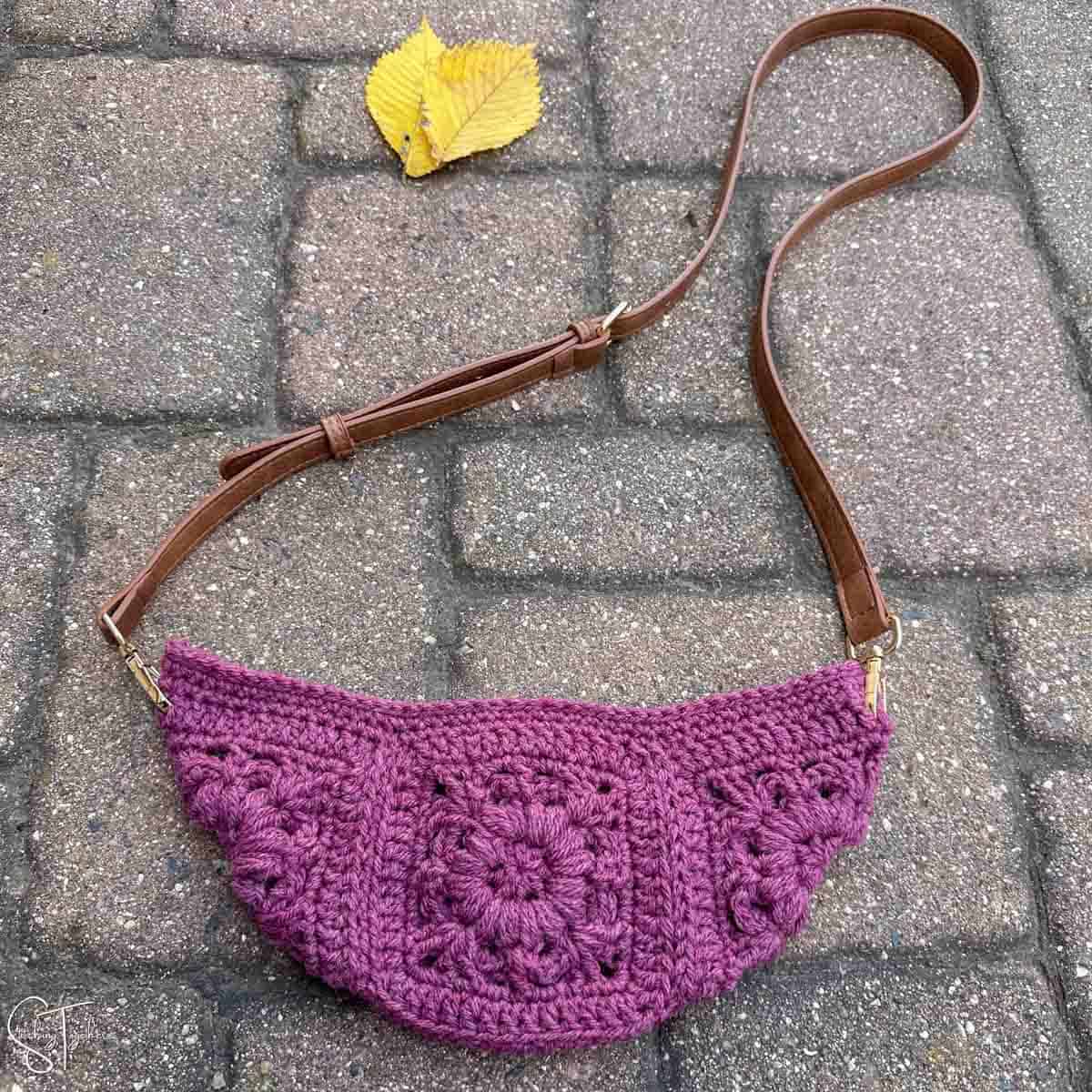 purple crochet bag made with granny squares and a leather strap laying flat