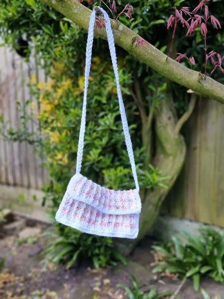 pink and white crochet purse hanging from a tree