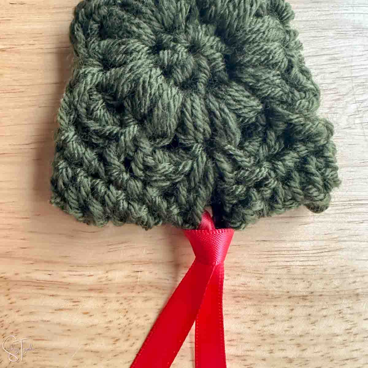 red ribbon attached to the bottom of a crocheted christmas tree