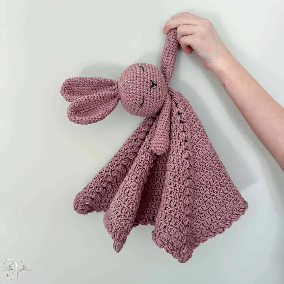 arm holding the hand of a pink crochet bunny lovey
