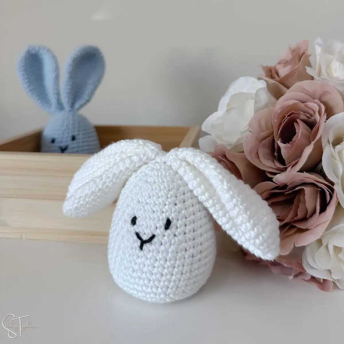 two easter egg crochet bunnies on a table. One of the bunnies is sitting in a little box