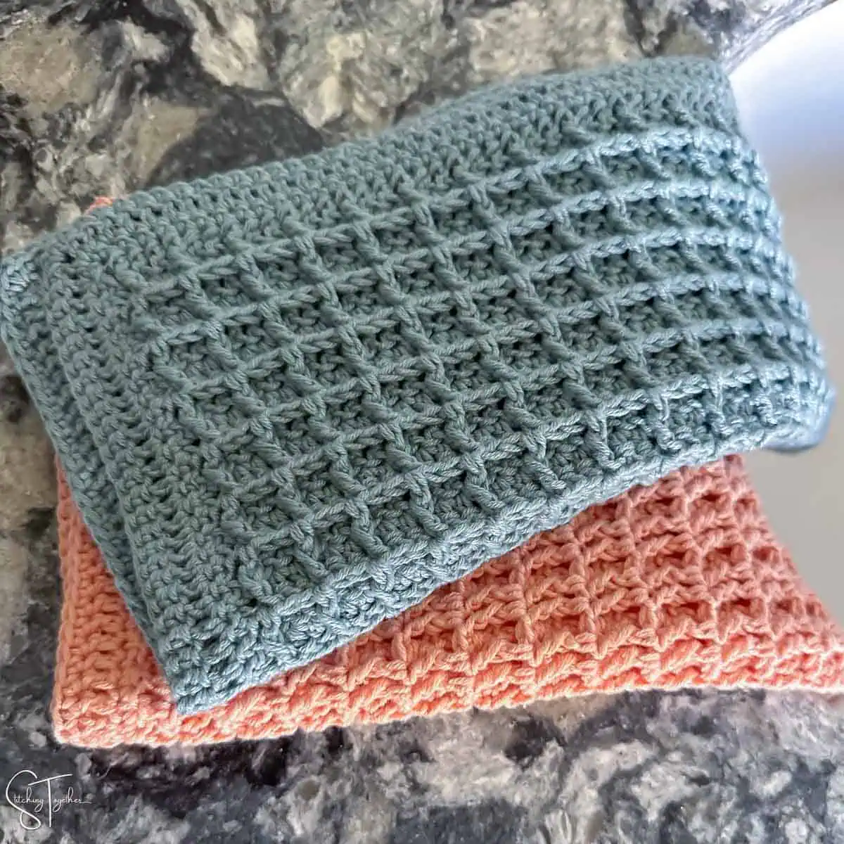 two waffle stitch crochet washcloths folded on the edge of a sink