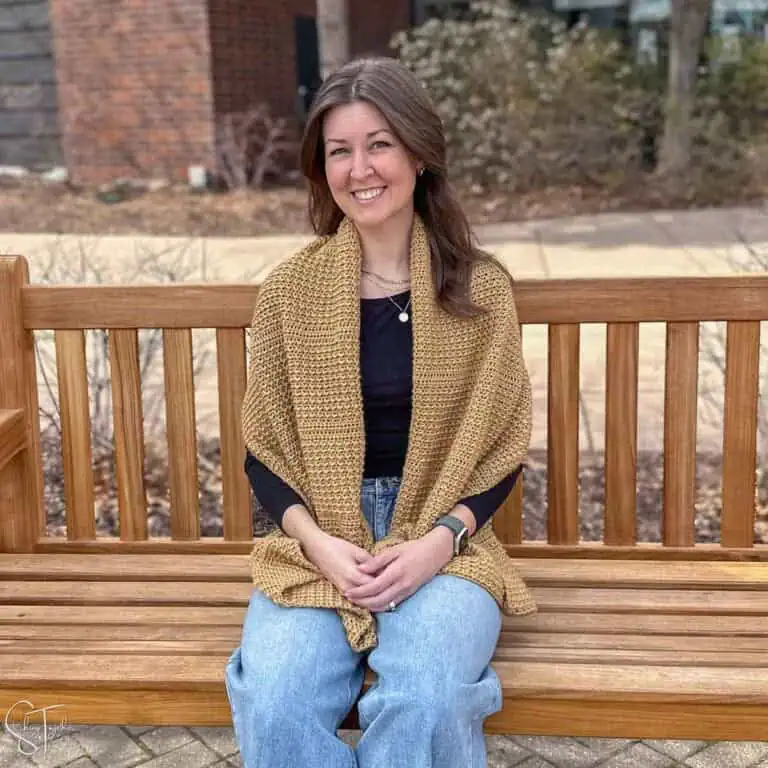 woman, wearing a crochet shawl while sitting on a bench