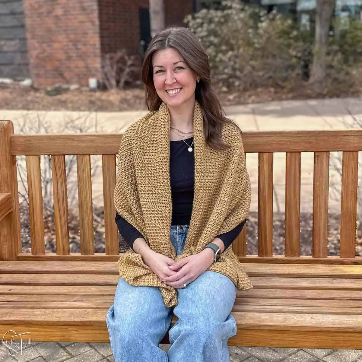 woman, wearing a crochet shawl while sitting on a bench