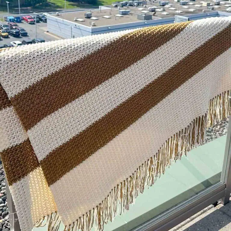 brownish and ivory striped crochet blanket draped over a railing