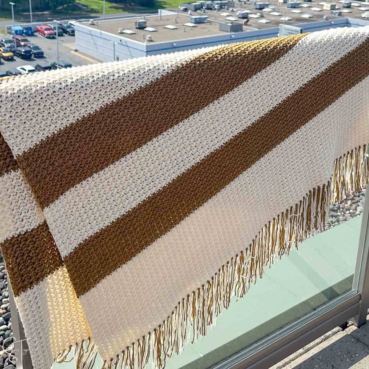 brownish and ivory striped crochet blanket draped over a railing