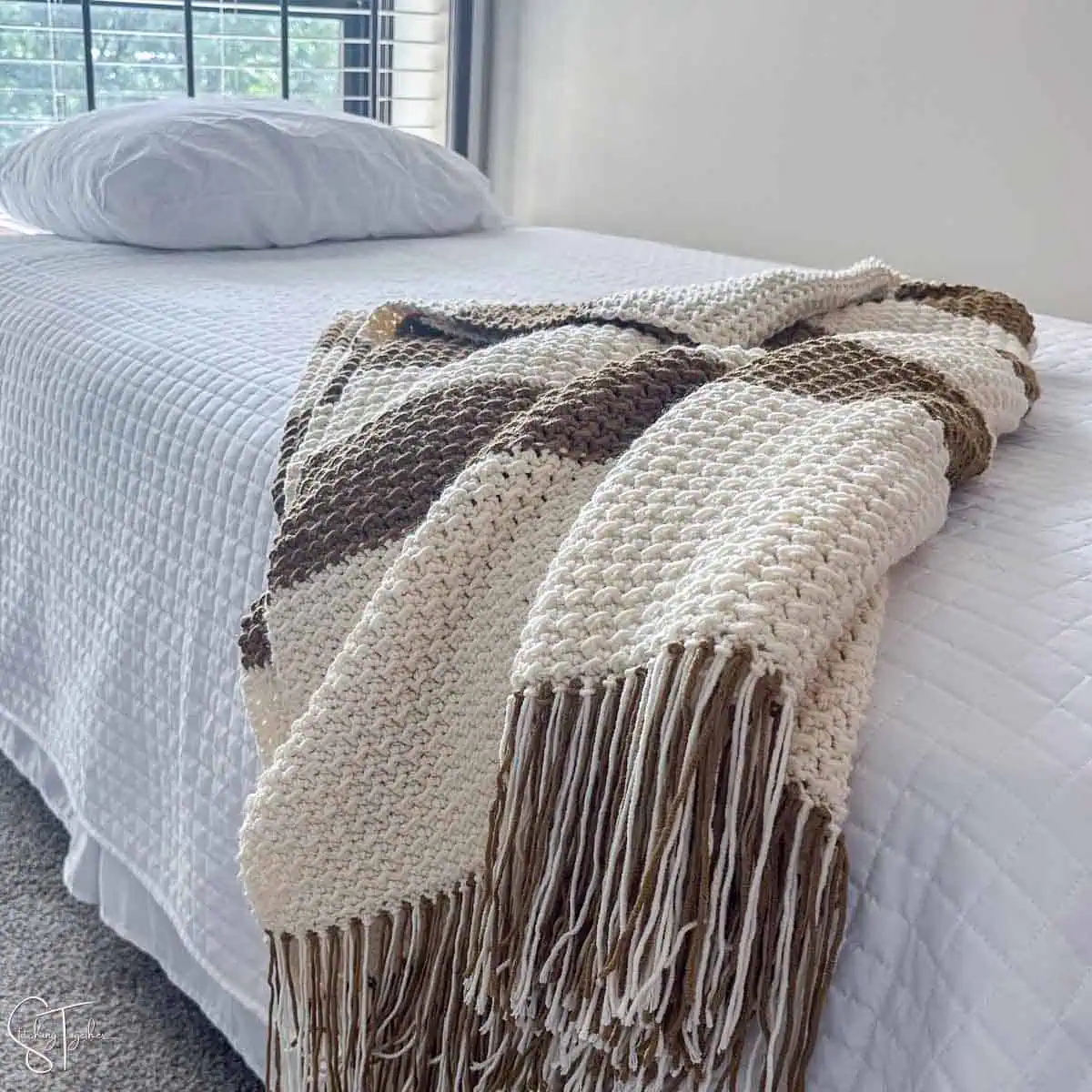 modern crochet blanket with stripes draped on a bed