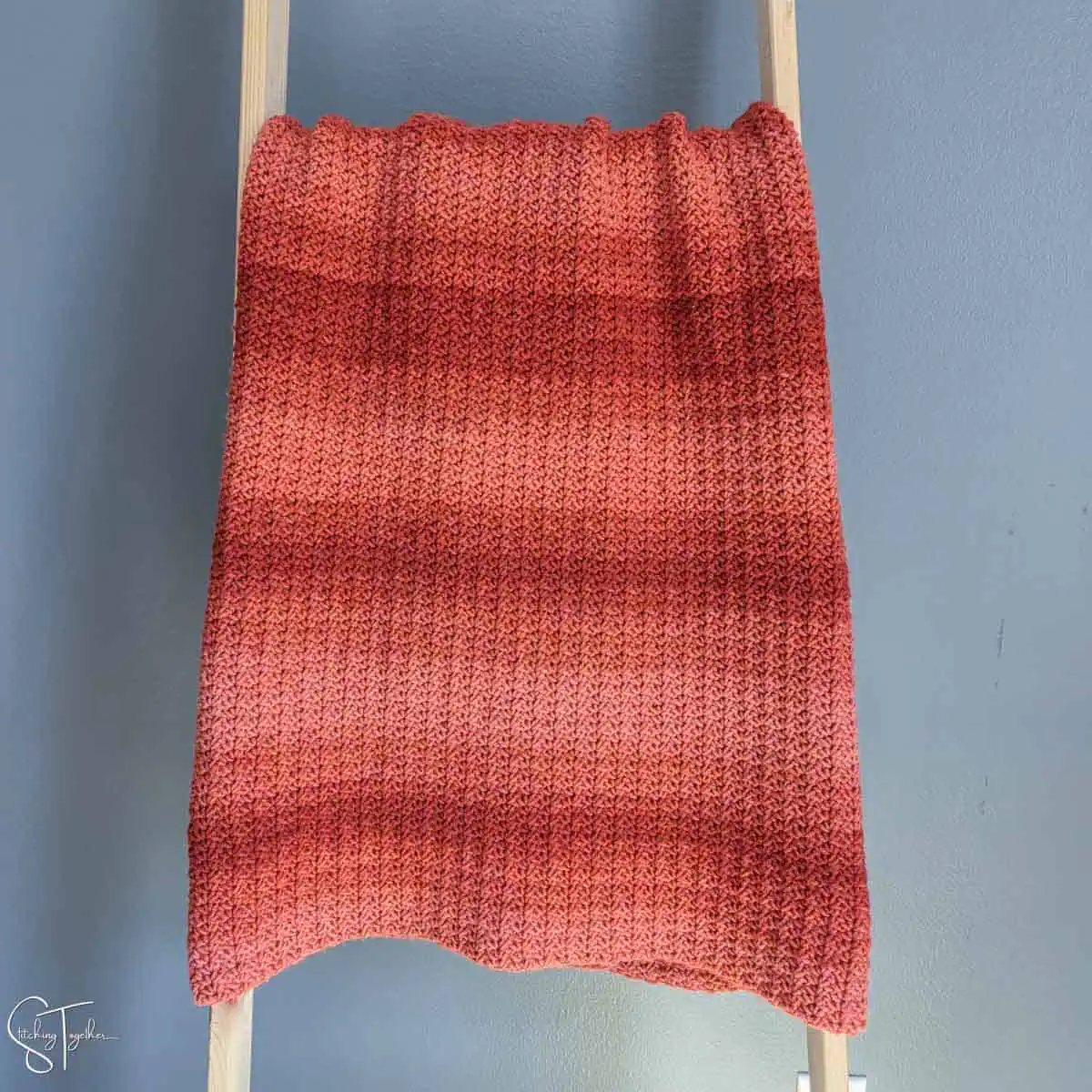 ombre orange crochet blanket draped on a ladder